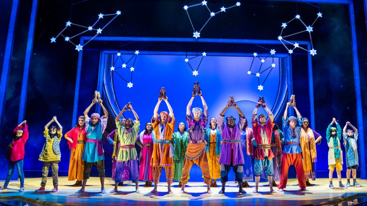 Group of people standing on a stage, dressed in colourful costumes.