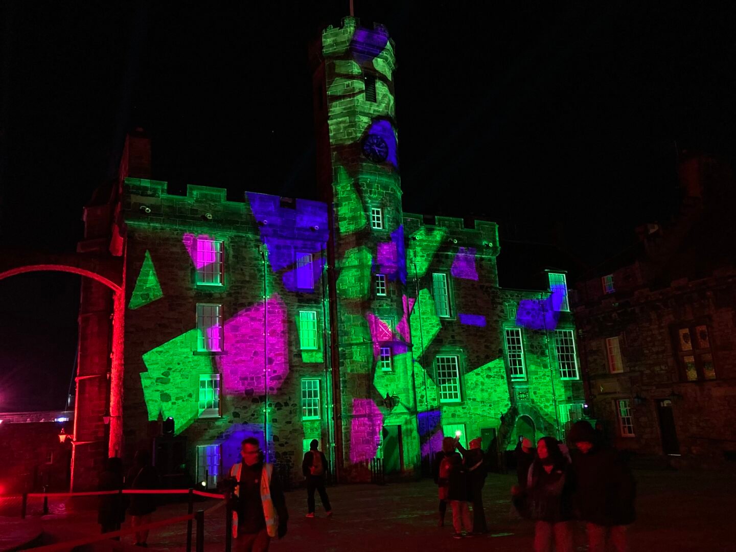 3 storey building with a central tower lit up with green, blue and link lights.