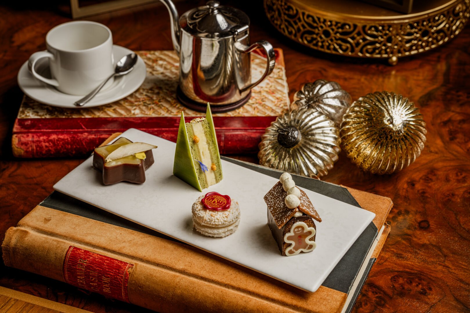 A table set with silver teapot, cup and saucer and a selection of cakes.