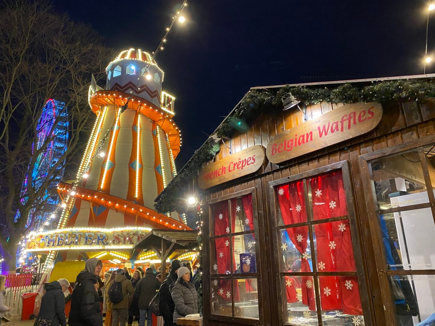 Night-time image of a stall selling crepes and waffles with a lit-up helter-skelter in the background.