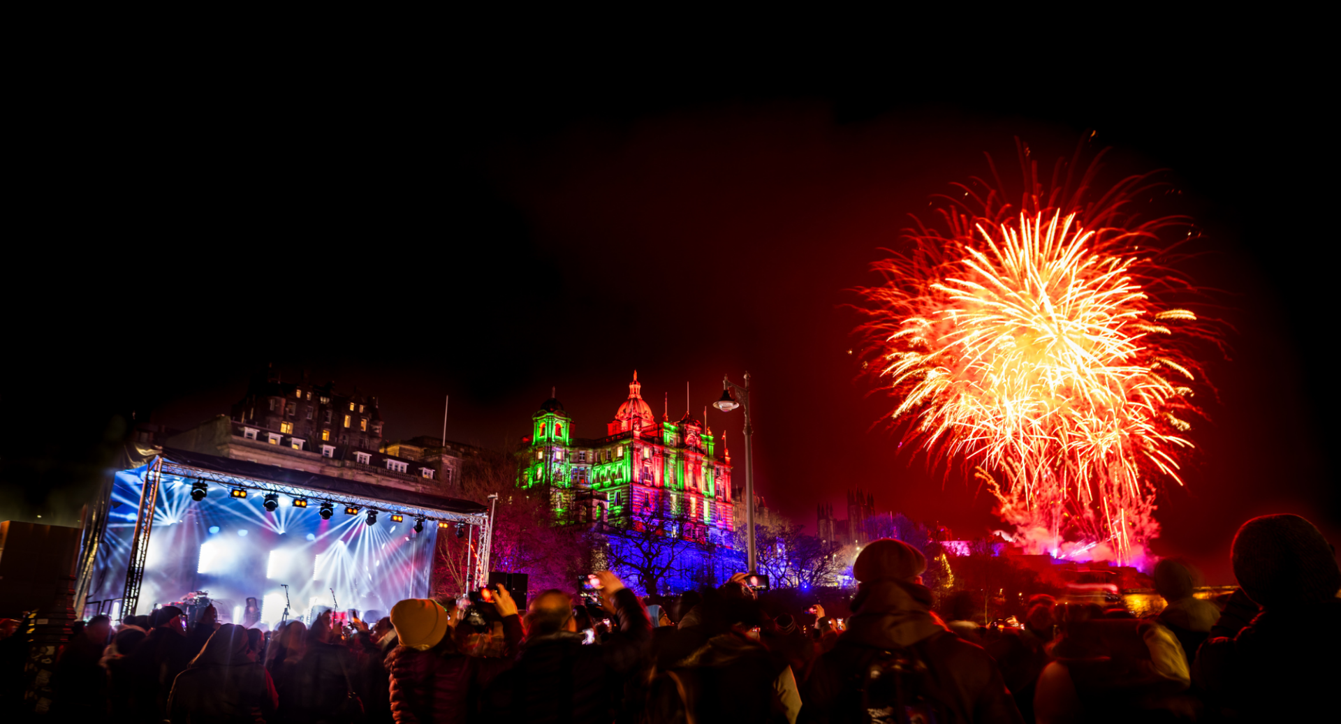 Crowd watching a bright red firework go off in sky.