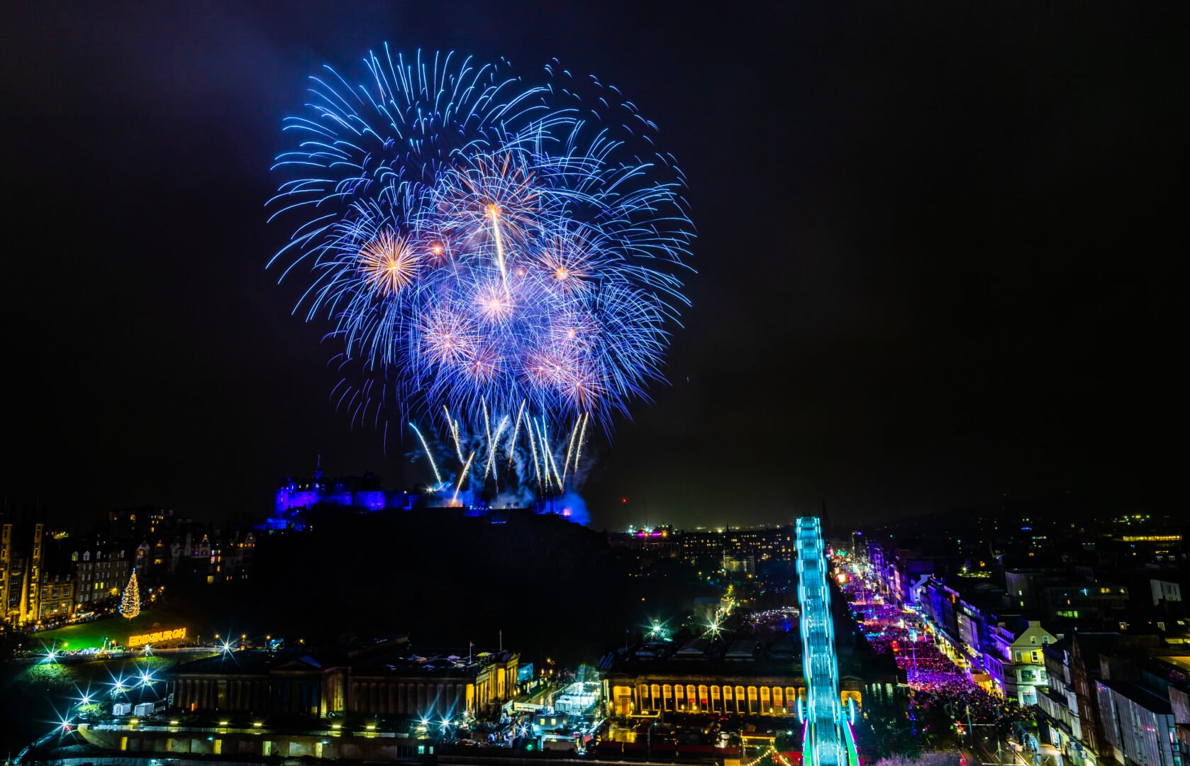 A blue coloured firework going off in sky above castle and street.