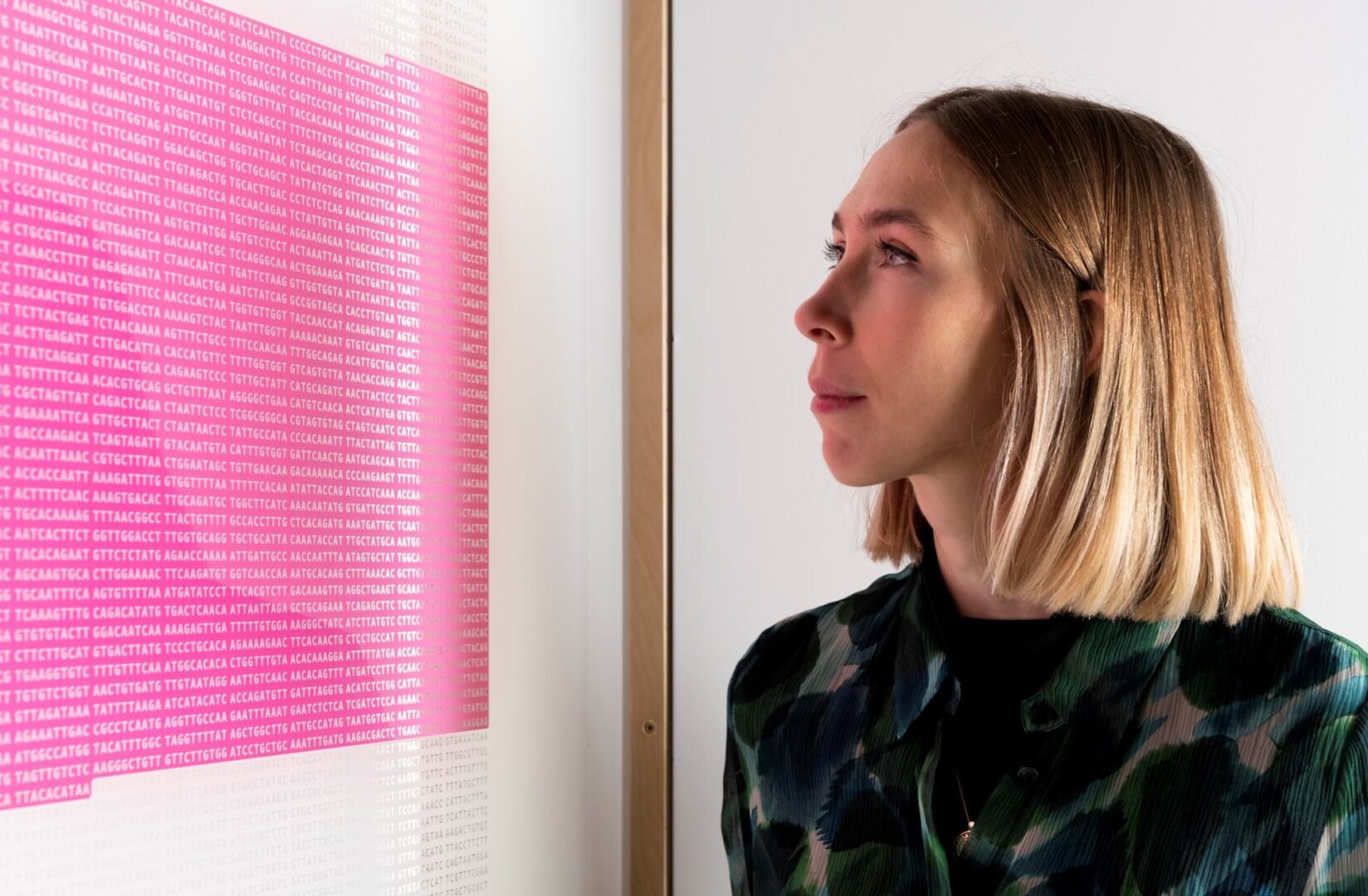 Women looking at a pink panel on the wall, which has lots of numbers and codes printed on it.