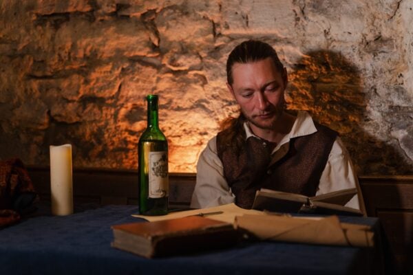 Guide sat at a table with candles, reading a book, dressed as Robert Fergusson at the Real Mary King's Close