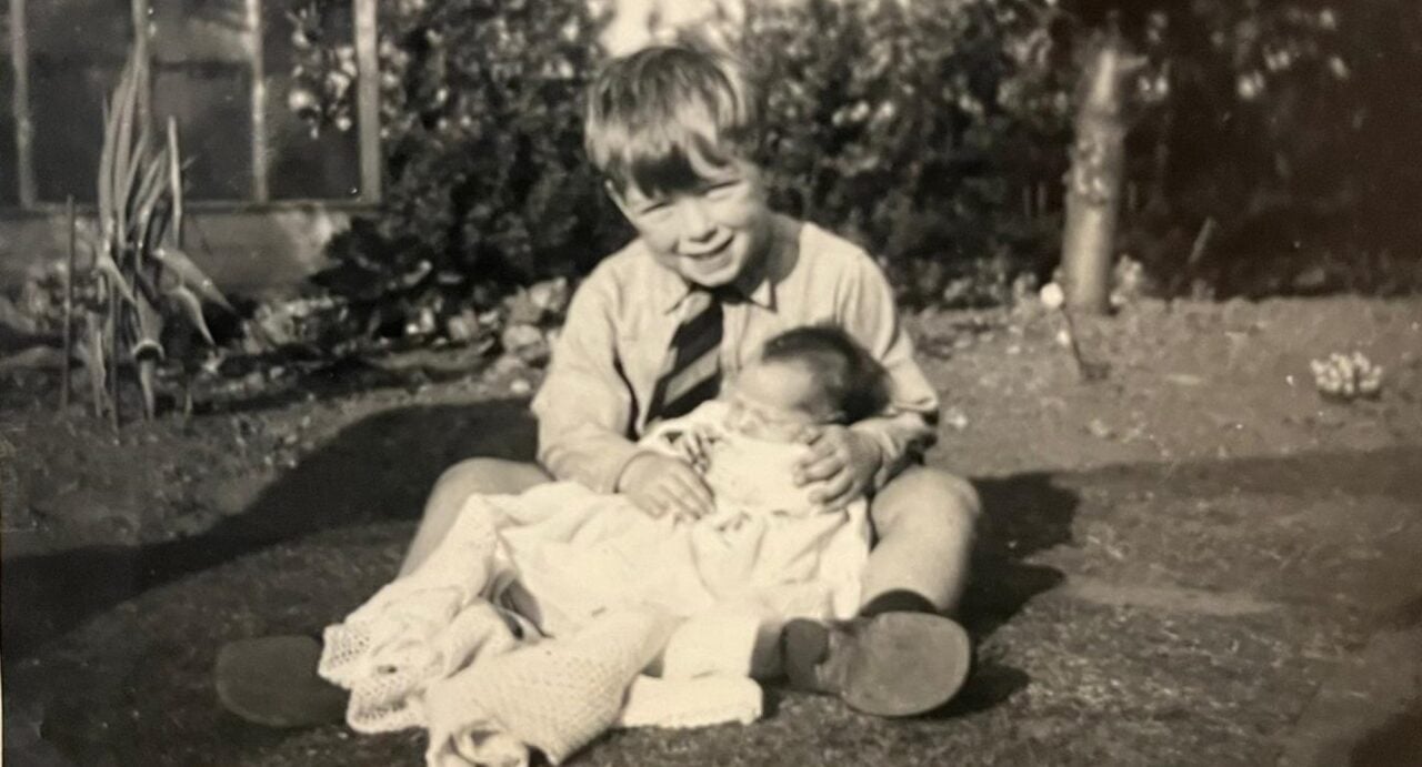 Gordon in his school uniform sitting in the garden with baby Frances in a shawl on his lap