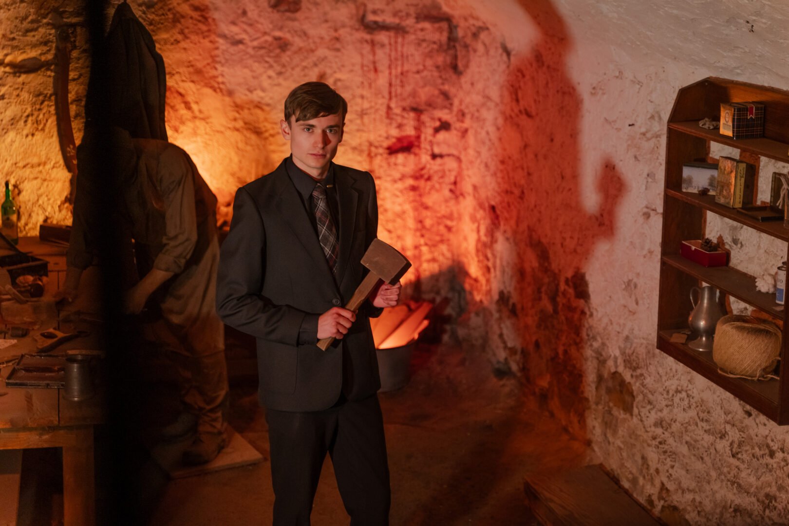 Man standing in dimly lit room, holding a mallet.