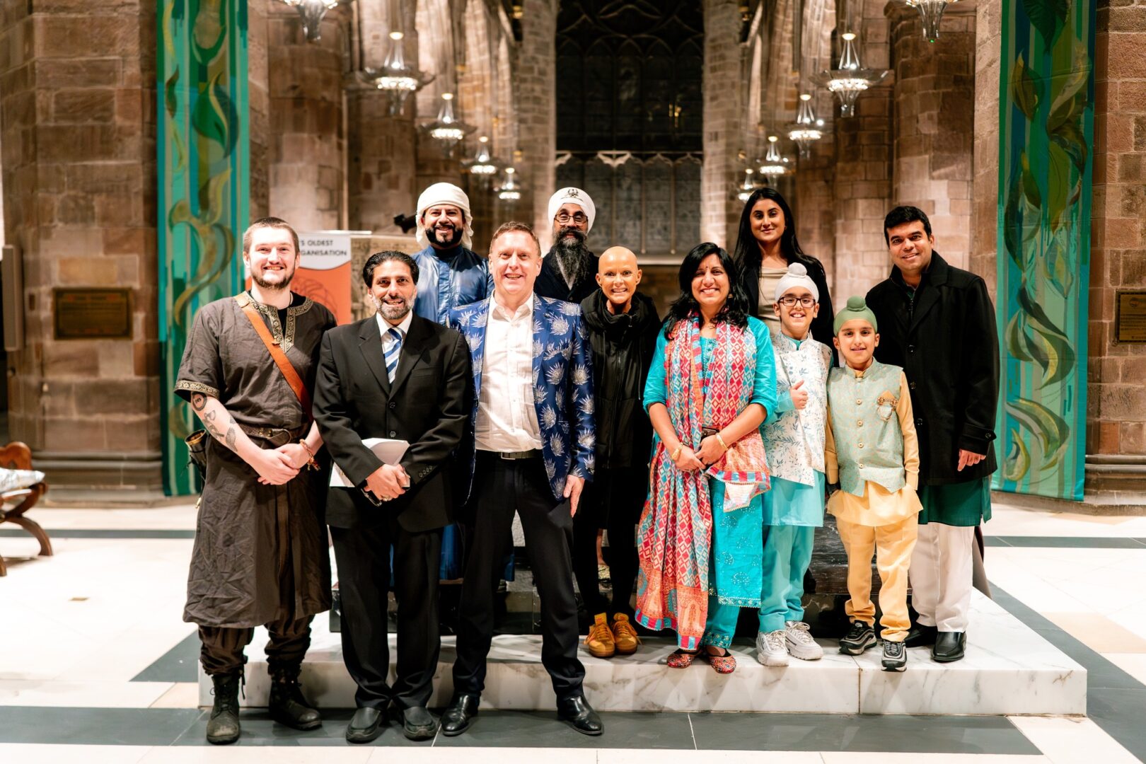 A group of people standing on a marble plinth inside a stone building with ceiling lights above, smiling at the camera