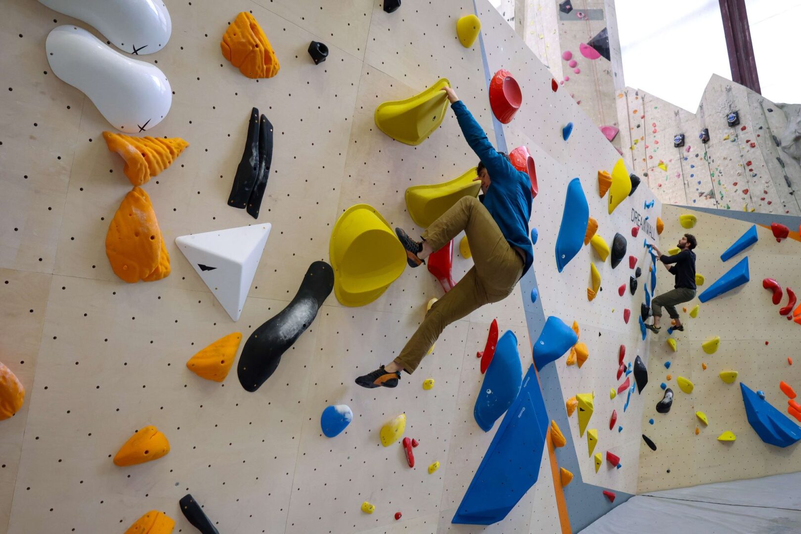 Person climbing a bouldering wall, which has lots of brightly coloured sections to hold onto.