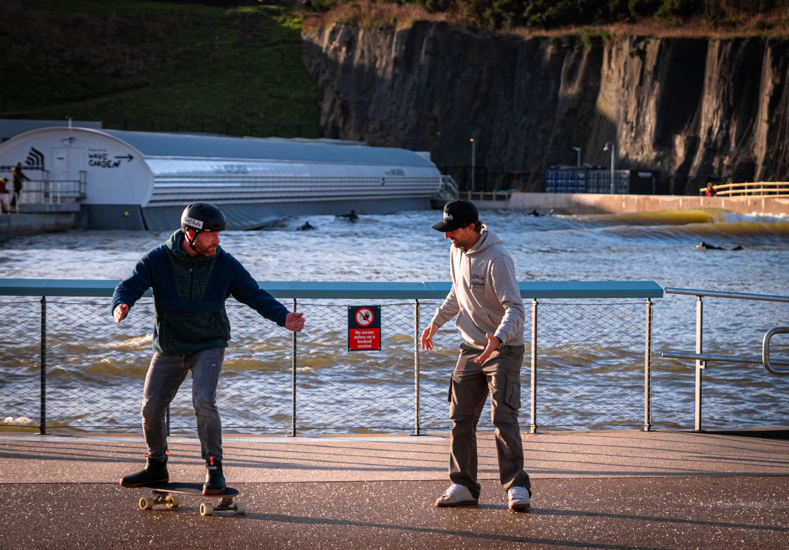 1 person showing another person how to surf skate.