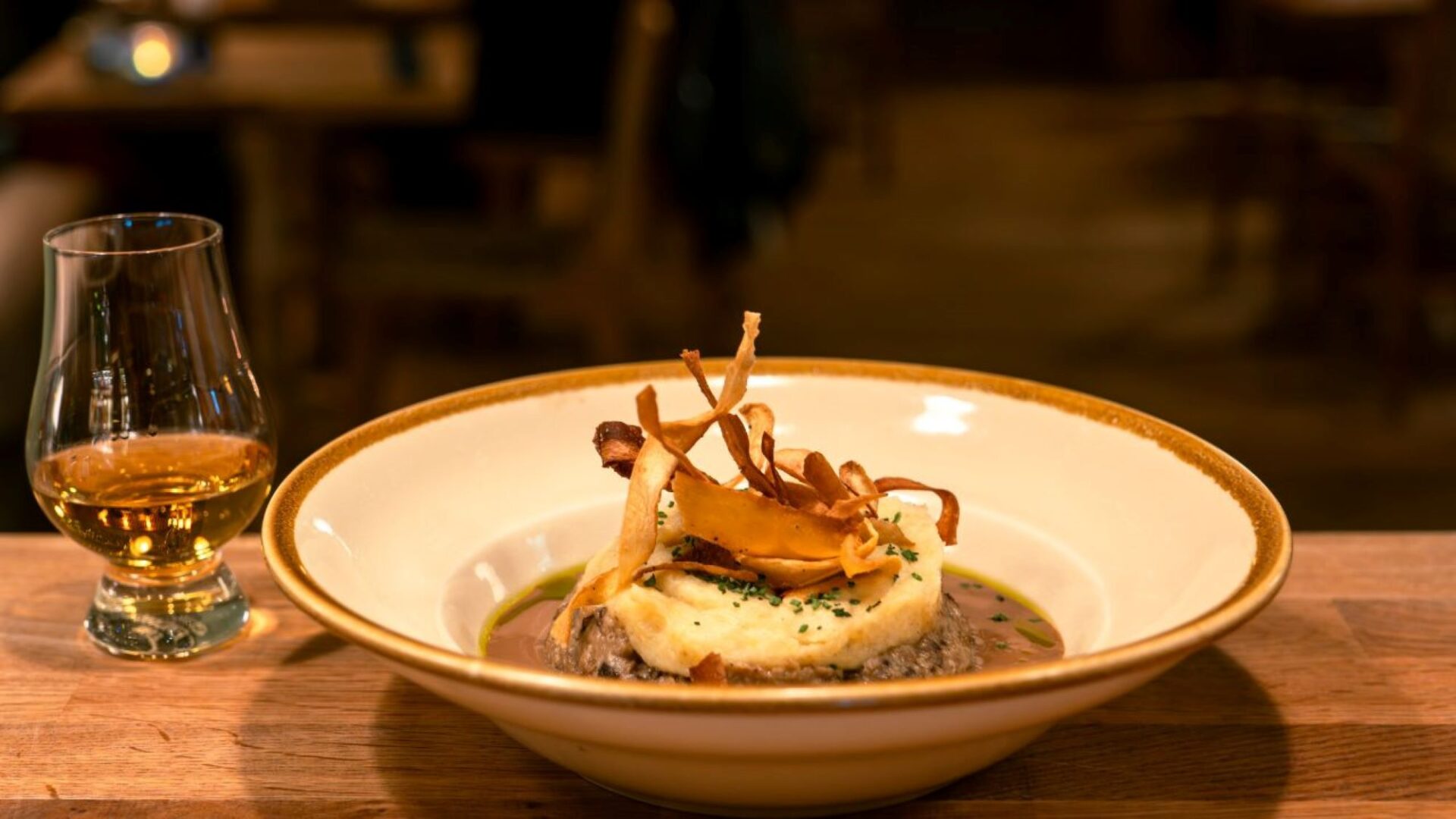 Bowl filled with haggis, mashed potatoes and turnip, sitting beside a glass of whisky.