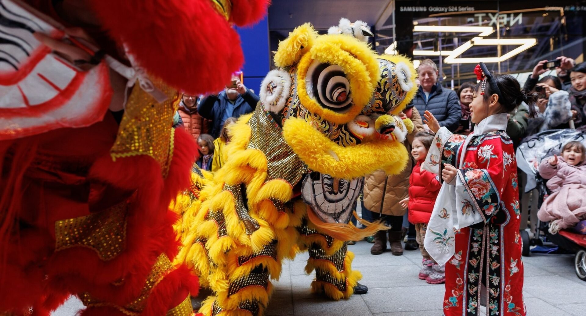 2 people in traditional lion costumes dancing in front of small girl in traditional Chinese clothing.