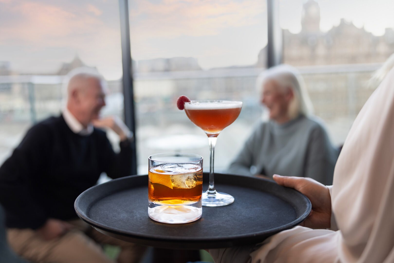 Couple sitting having a drink in Nor@ loft with Edinburgh in skyline in background.