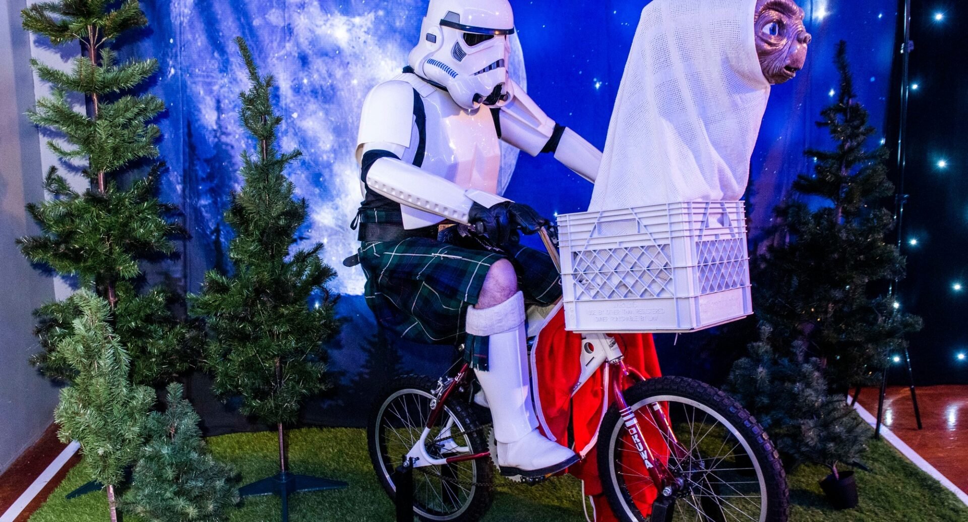 Stormtrooper from Star Wars wearing a kilt and riding a bike. In the bike's basket is ET.