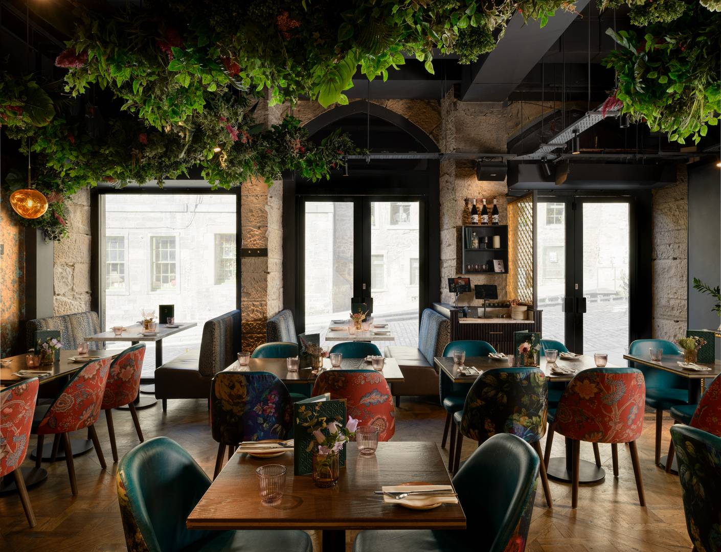 Luxury restaurant interior with stone walls, foliage adorning the ceiling and set tables with bright upholstered chairs. There are three windows with views out to Blackfriars Street.,© 3 Blind Mice - photography by ZAC and ZAC