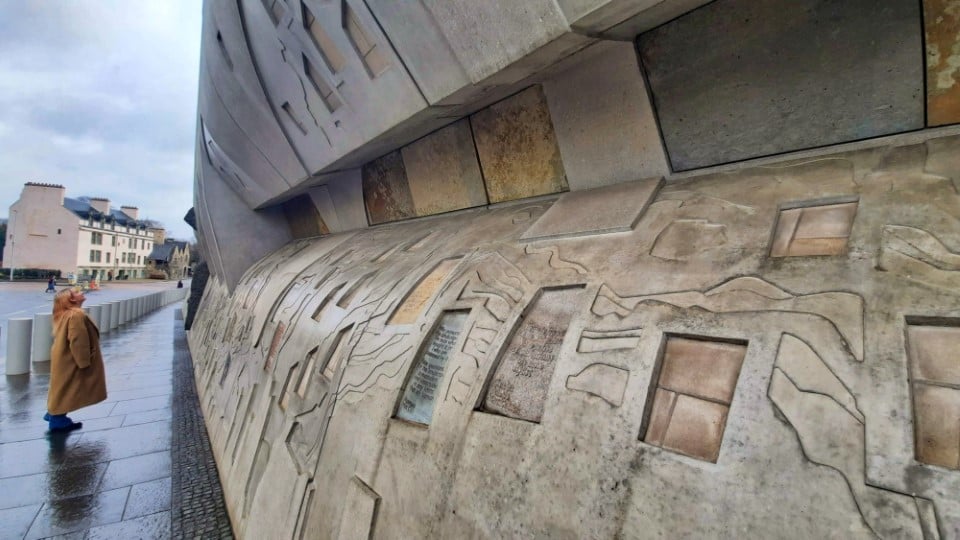 A woman standing on the pavement looking at the inscriptions on the Canongate wall