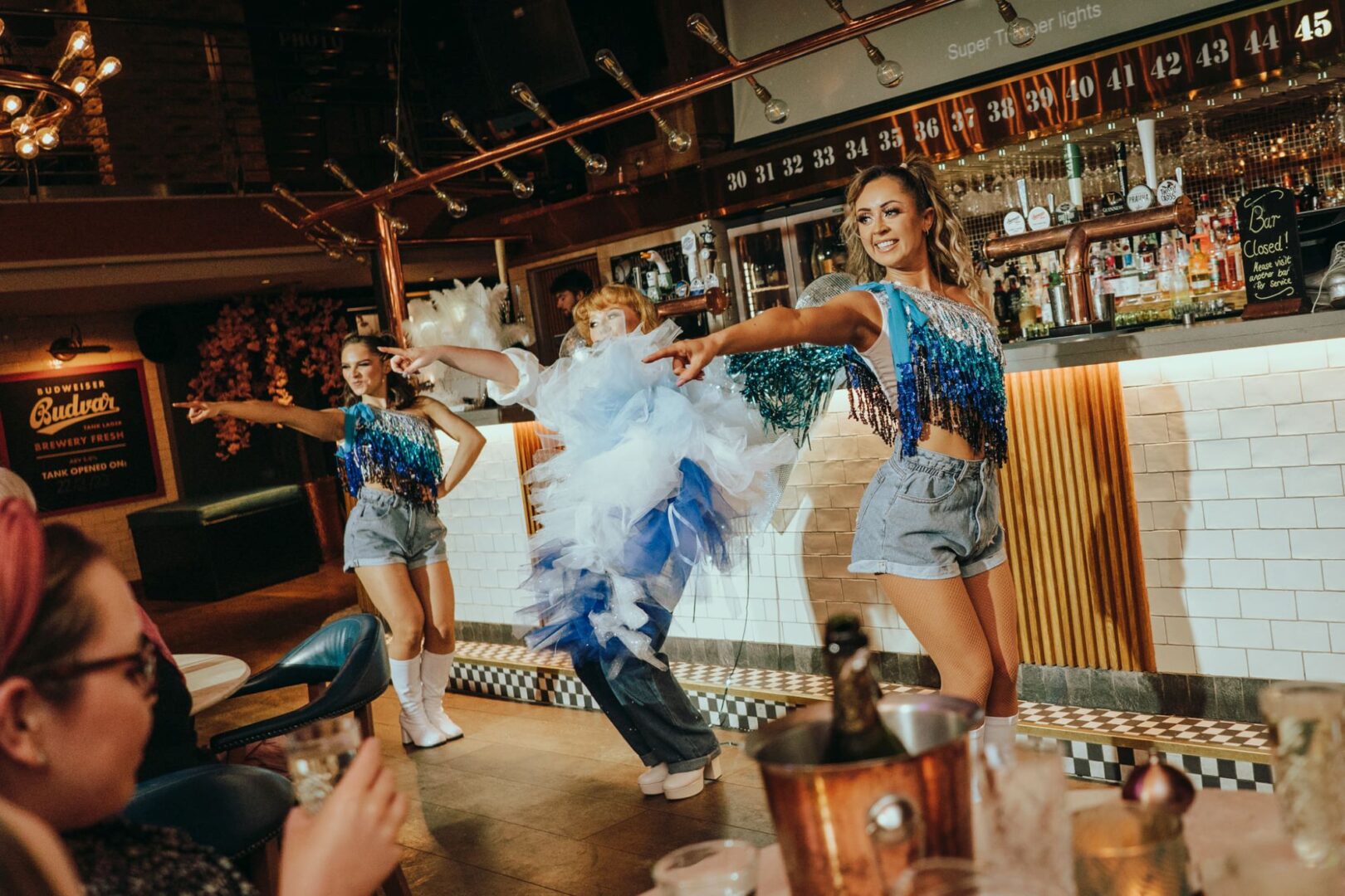 3 people standing in front of a bar, dancing to a crowd of people.