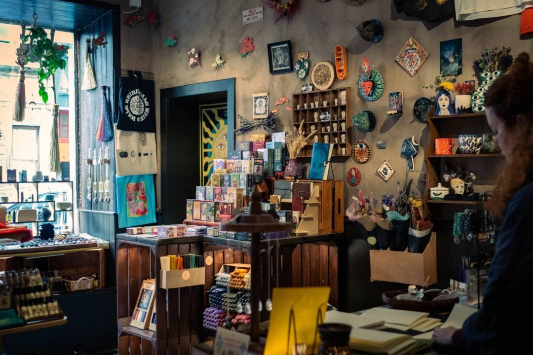 a bright window shines light on a wall display of ceramics, tote bags, crystal sun catchers, brooms, tarot decks, and spell candles