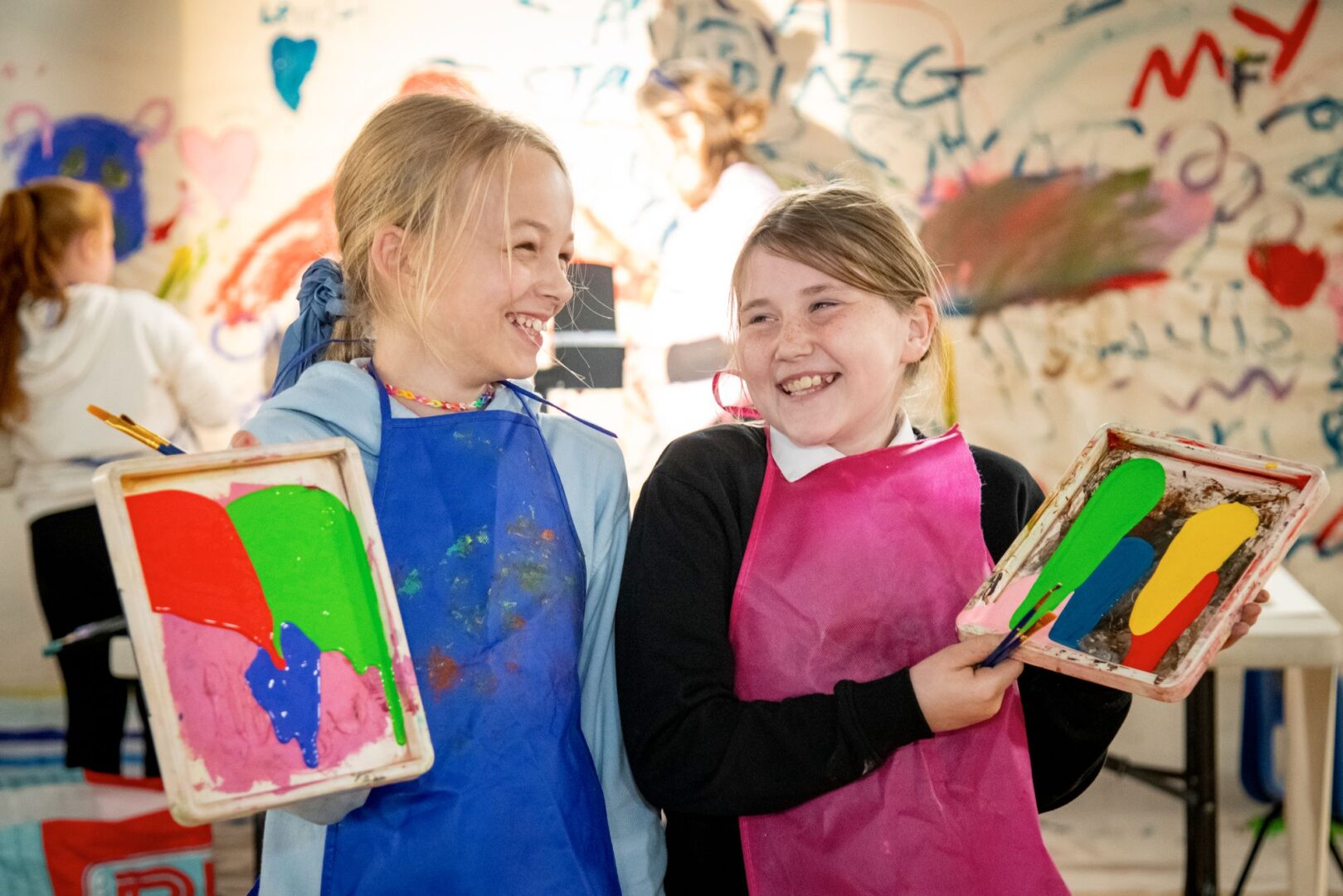 2 young girls holding paintings and brushes.