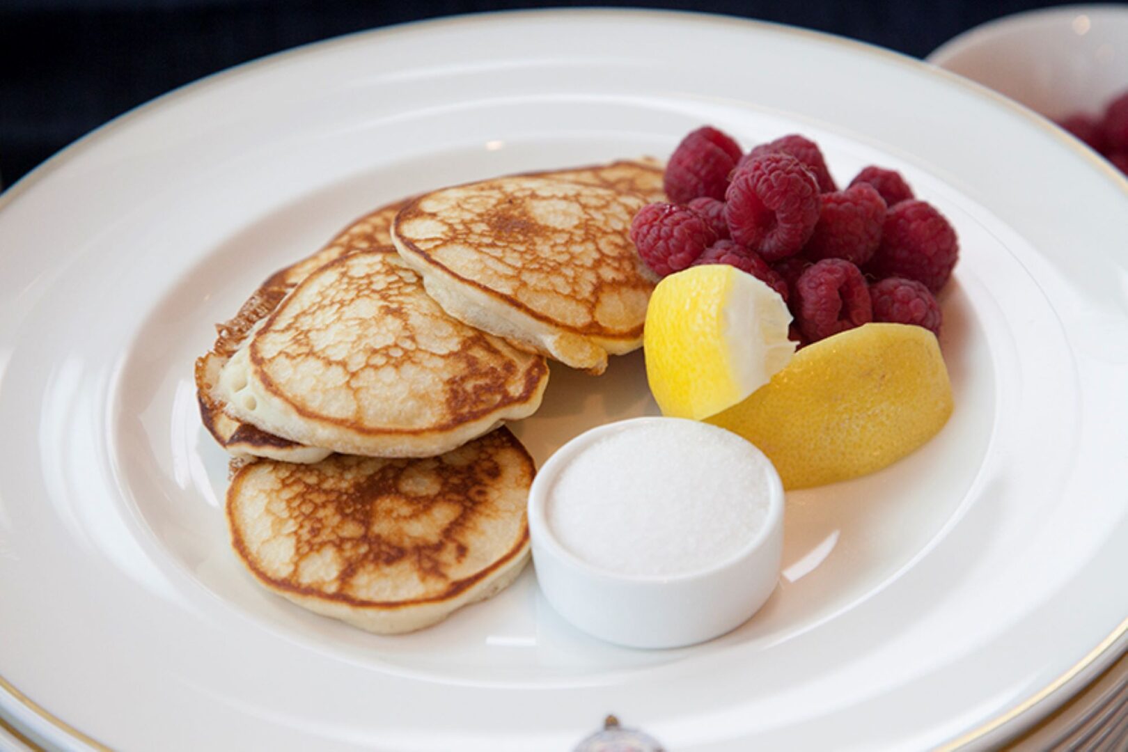 Plate of pancakes, with raspberries, sugar and lemons wedges.