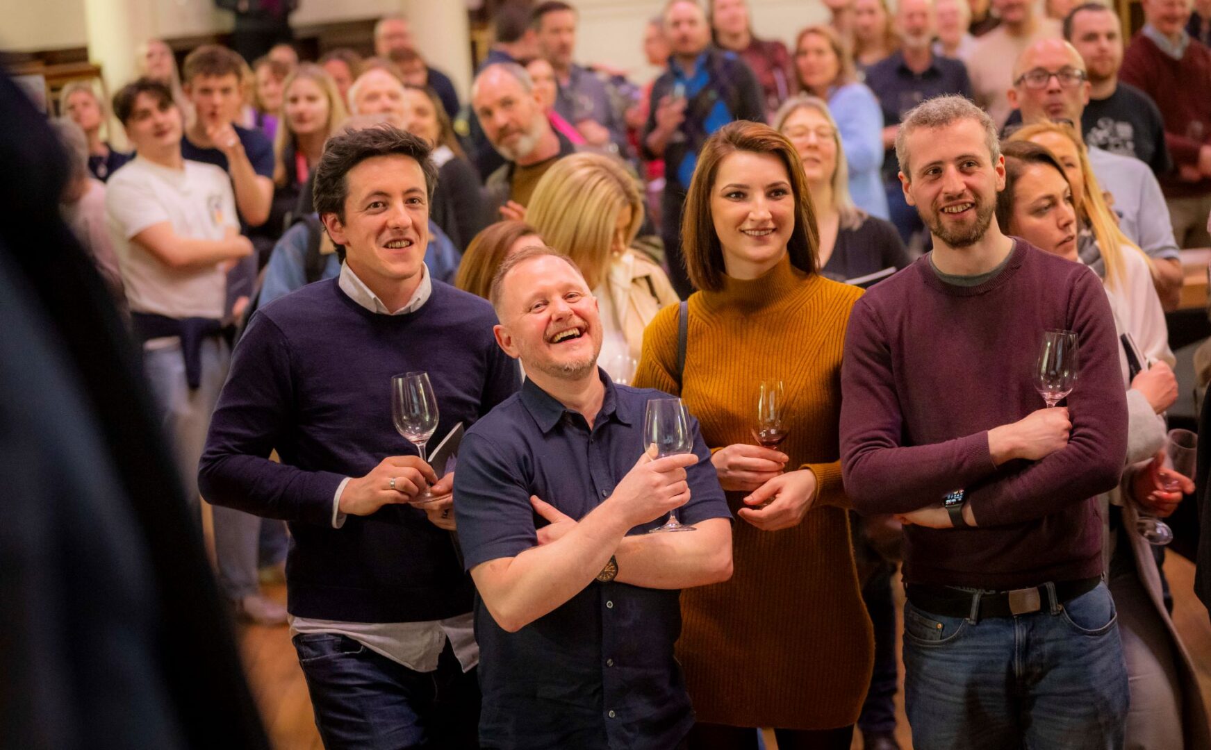 Group of people standing in a crowded room, all holding wine glasses.