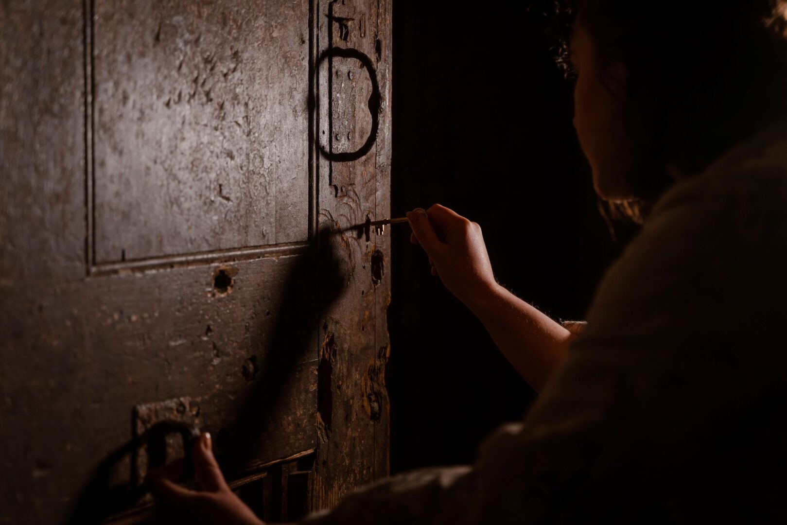 Low lit image of silhouette of person opening old fashioned door with a key.