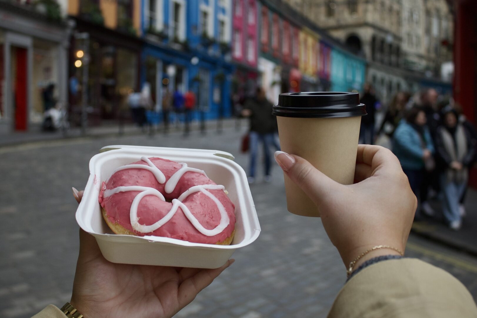 A hand holding a coffee cup and a doughnut in a box with busy Victoria Street in the background