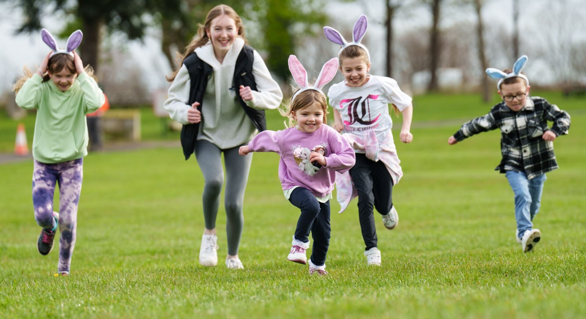 5 young children wearing bunny ears running across grass