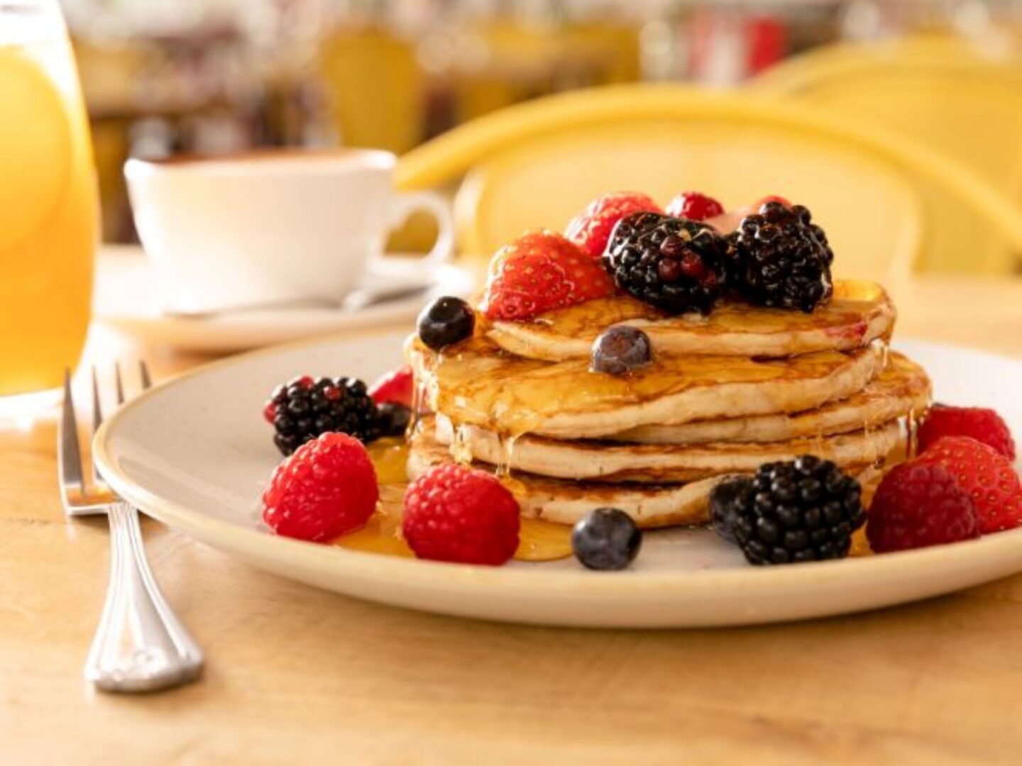 Pile of pancakes on a plate, with syrup, strawberries, raspberries and blackberries.