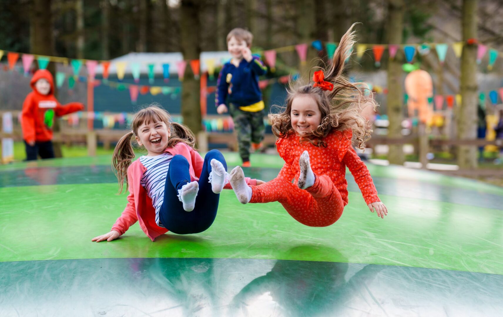 2 young girls bouncing and laughing on an outdoor bouncy surface.