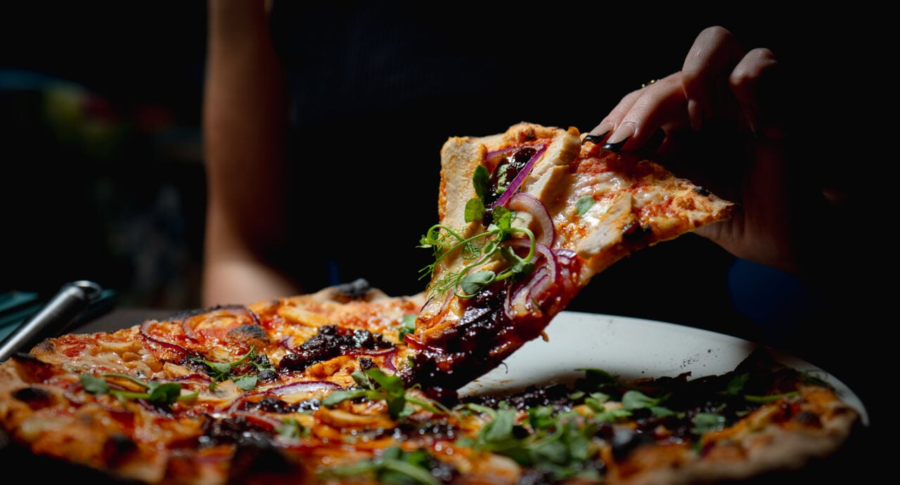 Hand lifting pizza of plate ©3 Blind Mice
