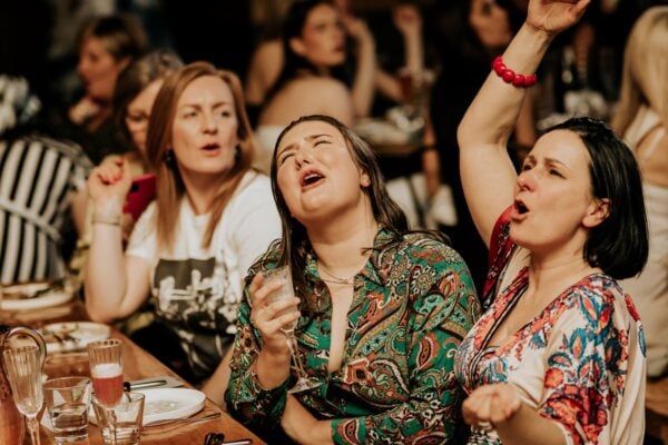 Table of women singing enthusiastically and waving their hands in the air.