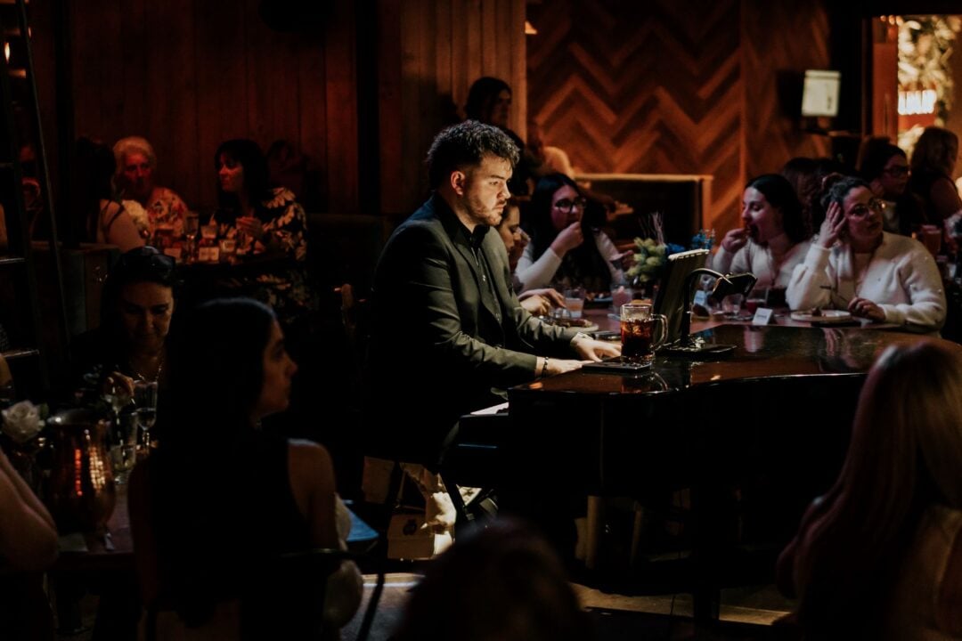 Man playing a grand piano in a crowded bar.