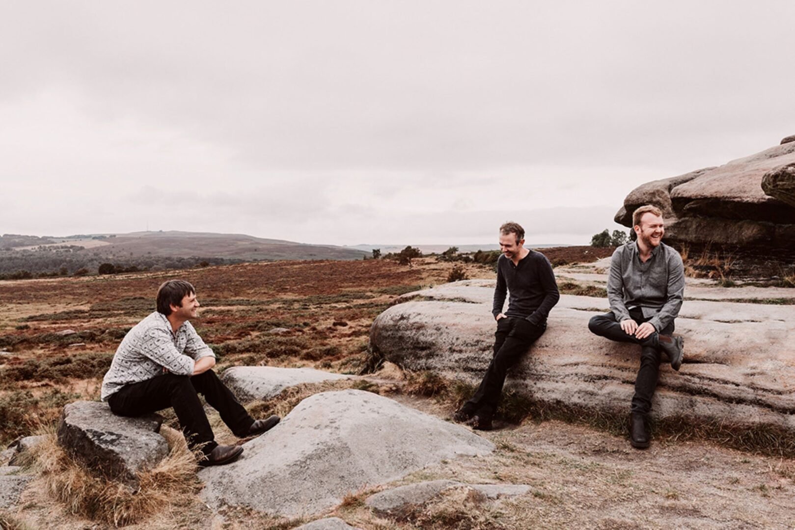 3 men sitting on large stone boulders amongst a mountainous landscape.