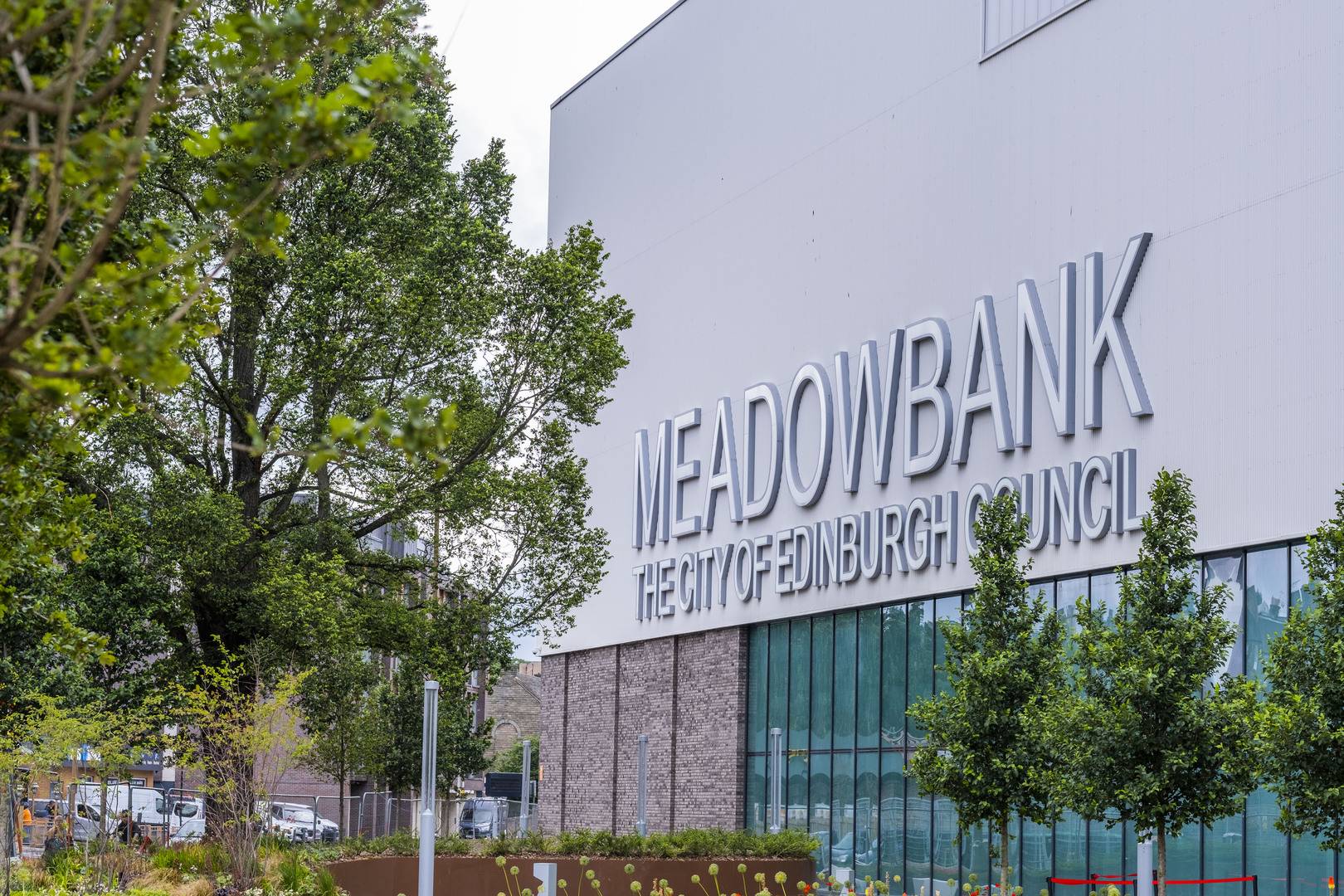 The exterior of Meadowbank Sports Centre in Edinburgh with large letter signage saying MEADOWBANK THE CITY OF EDINBURGH COUNCIL.  Green trees frame the picture,© Edinburgh Leisure