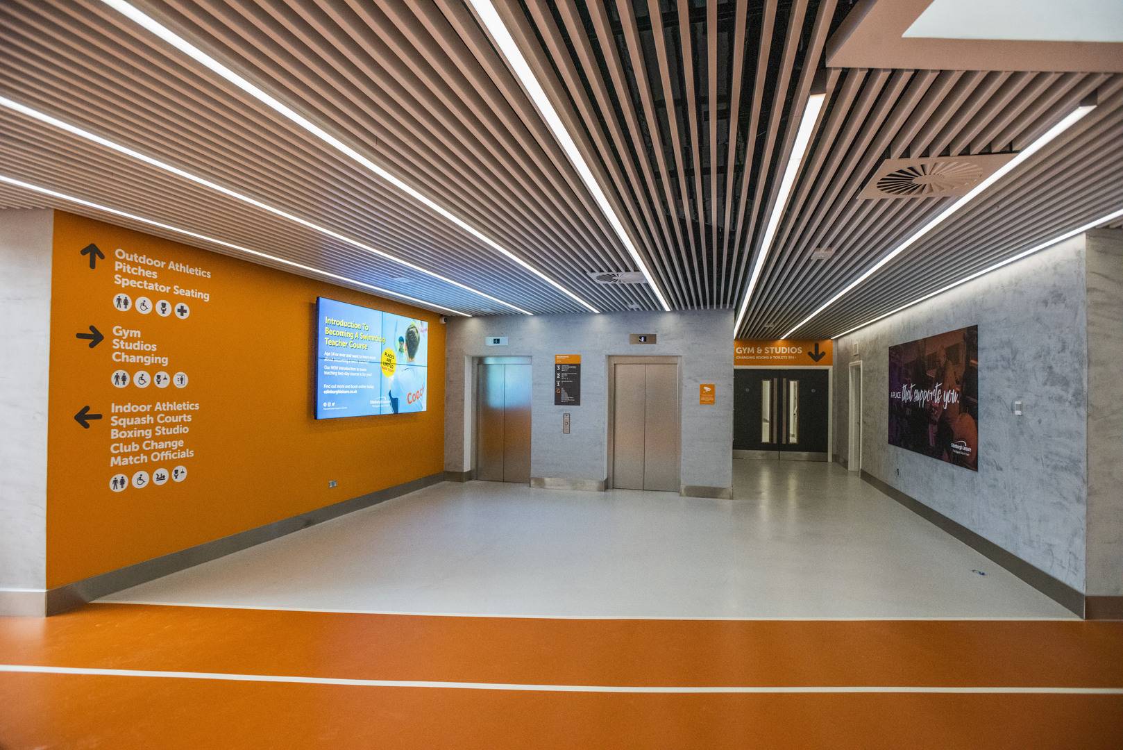 the interior of Meadowbank Sports Centre with a large LED screen promoting membership offers is on the wall, near to the two lifts.,© Edinburgh Leisure