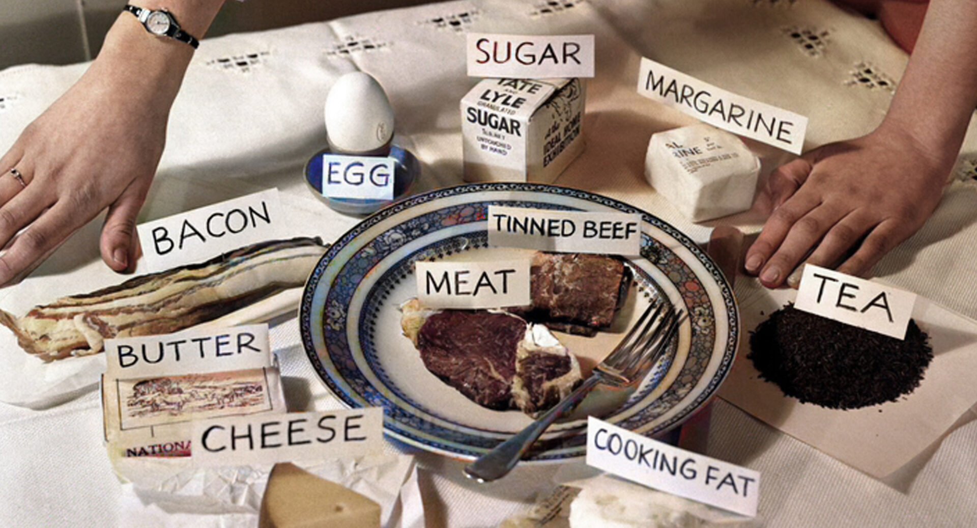 Table laid with various food items, all of which are labelled, such as egg, sugar, margarine, tea and cooking fat.
