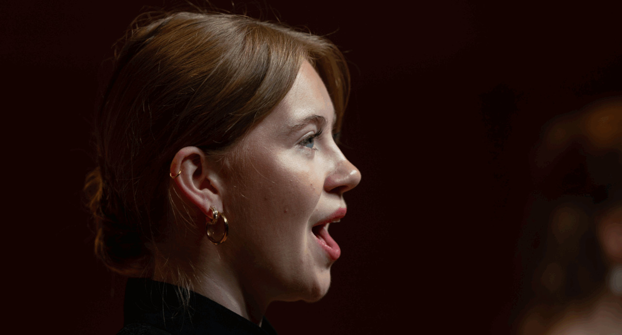 Side head view of a young woman singing.