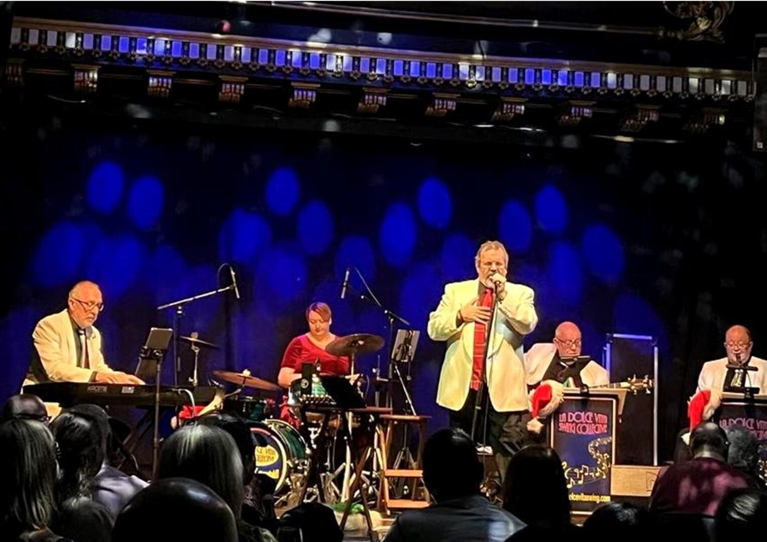 Man singing into microphone on a stage and a band behind him