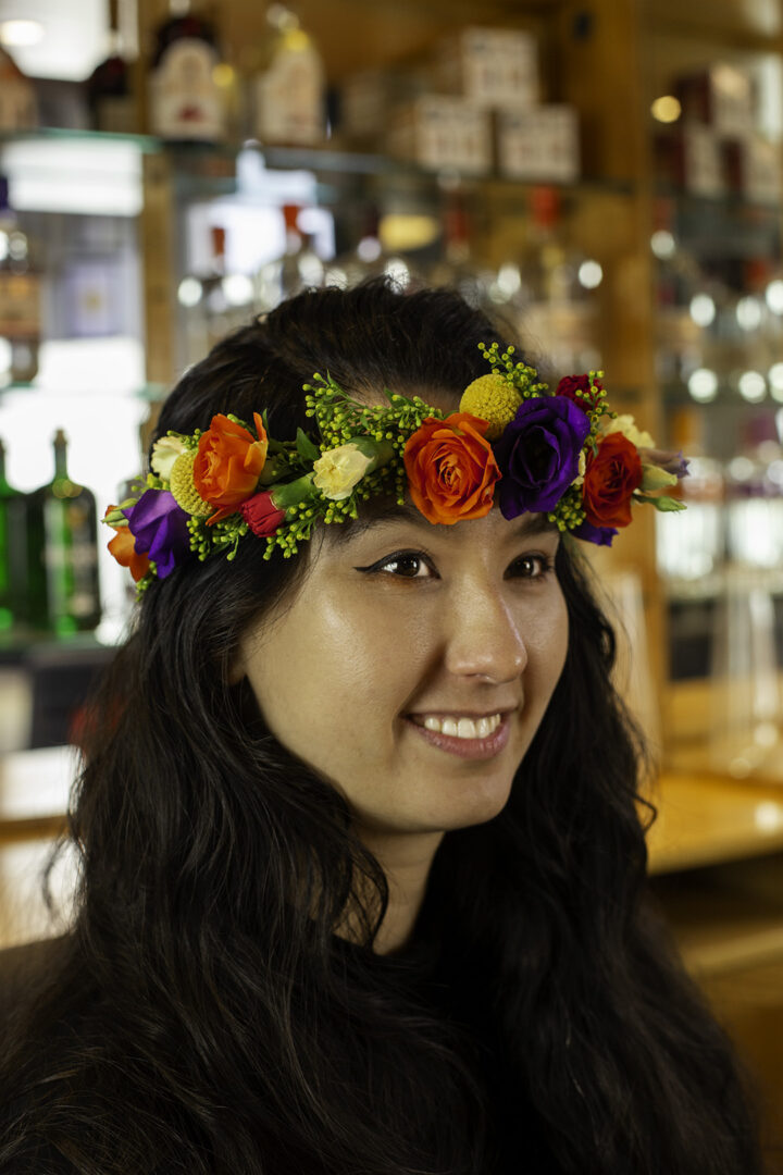 Woman with long dark hair wearing an orange, yellow and purple flower crown.