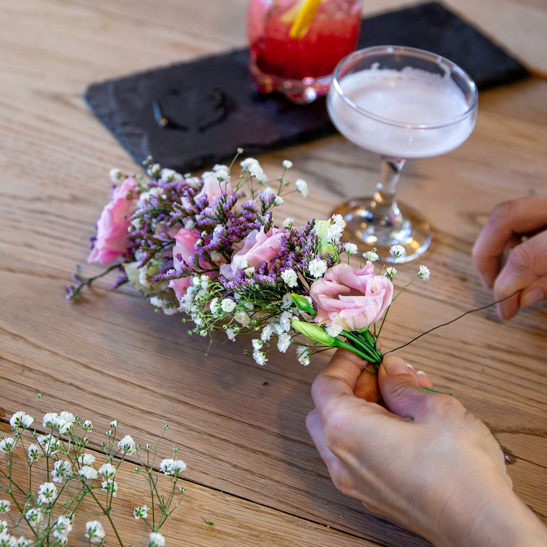 Pair of hands making a flower garland, with a drink at the side.