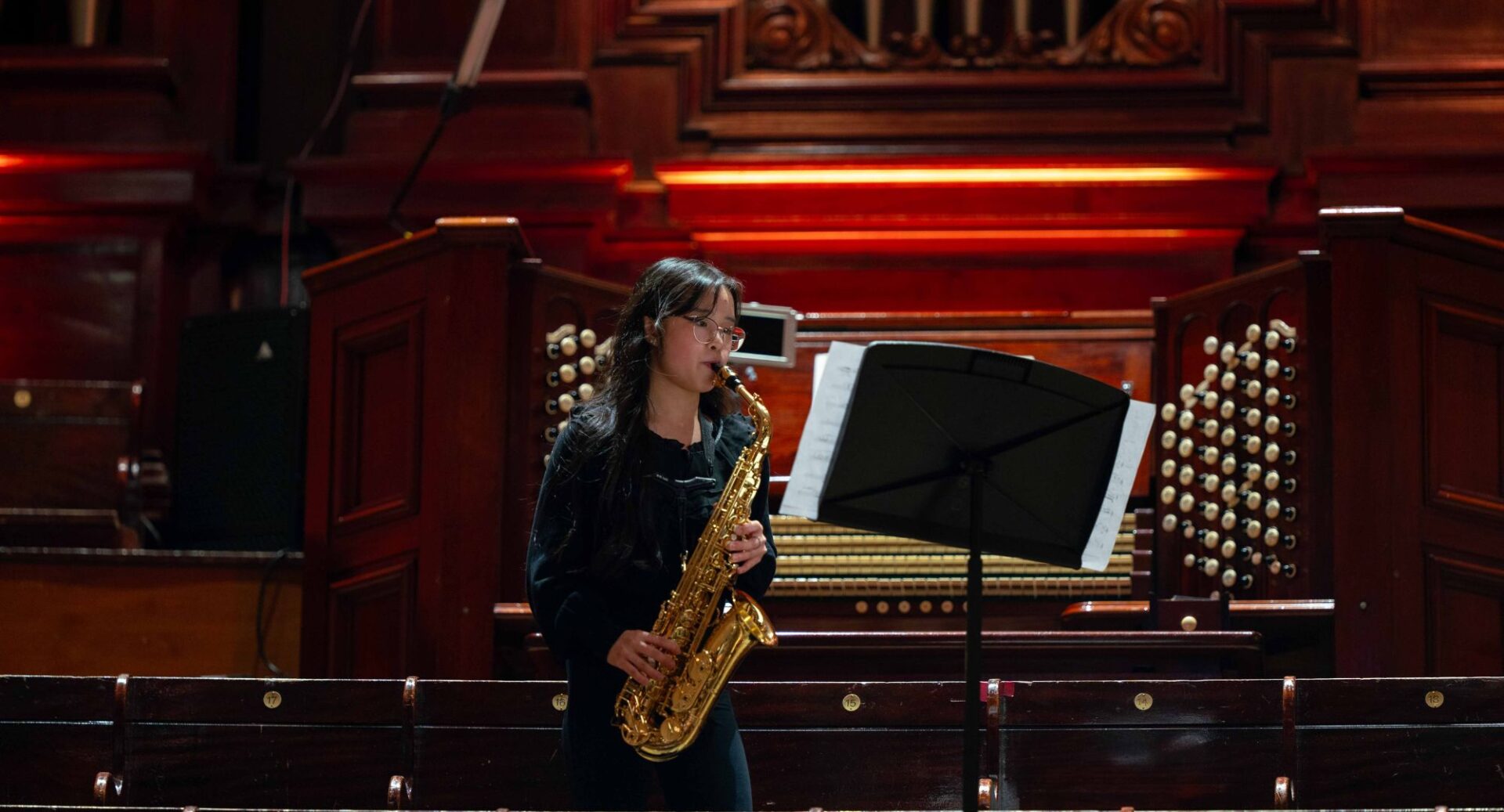 Young girl playing a saxophone. In the background is a music organ.