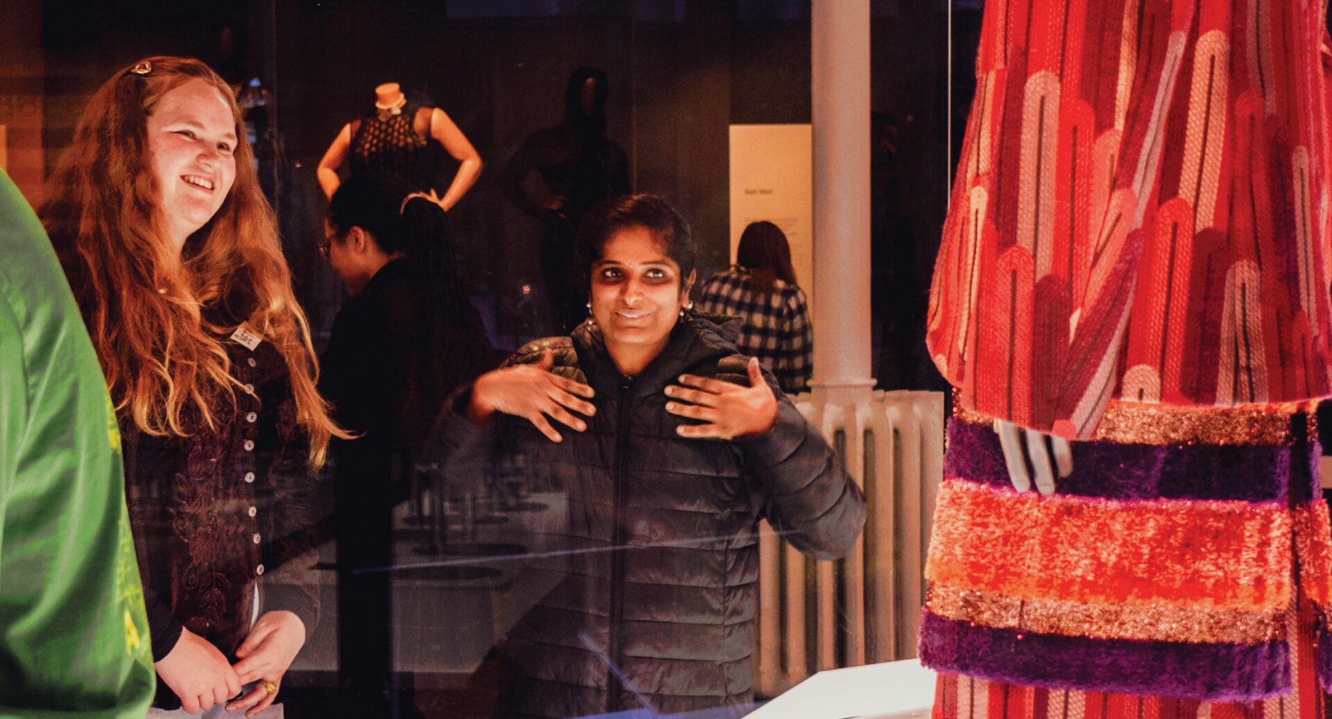 Two women looking at an orange and purple garment inside a glass case