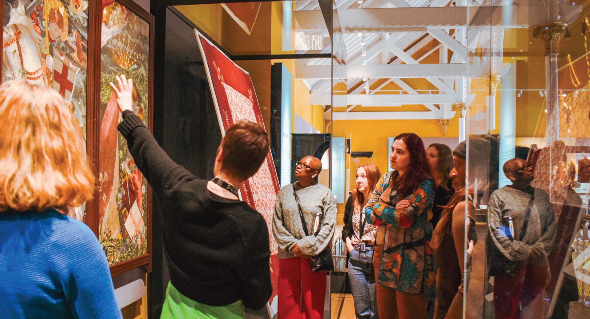 A group of women looking at an exhibit on the wall, possibly a tapestry, as the guide tells them about it