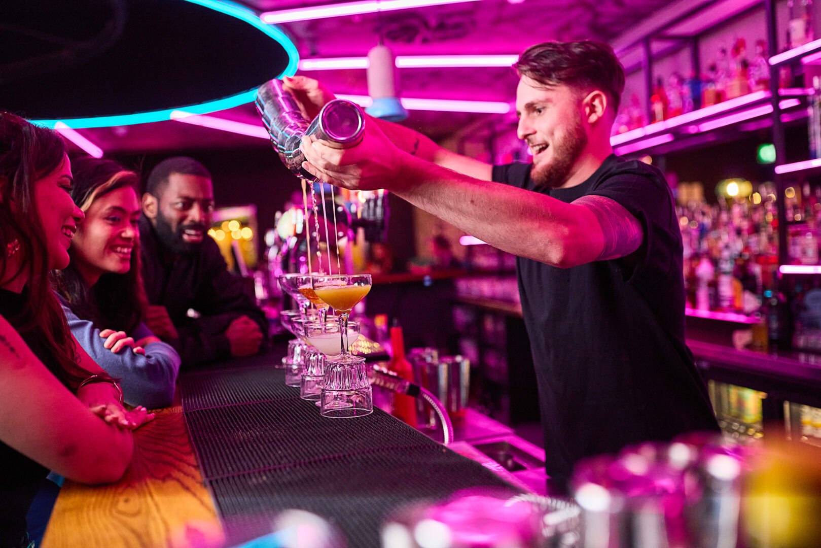 Bar person pouring cocktails with customers at bar watching