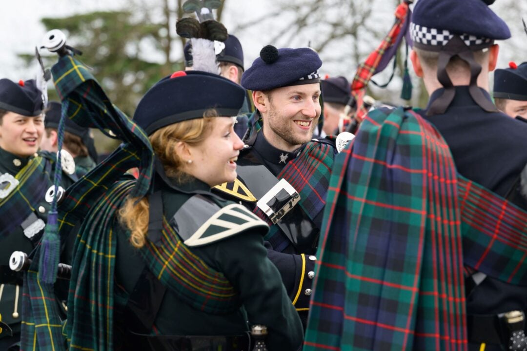 Group of people holding bagpipes and wearing traditional Scottish dress.