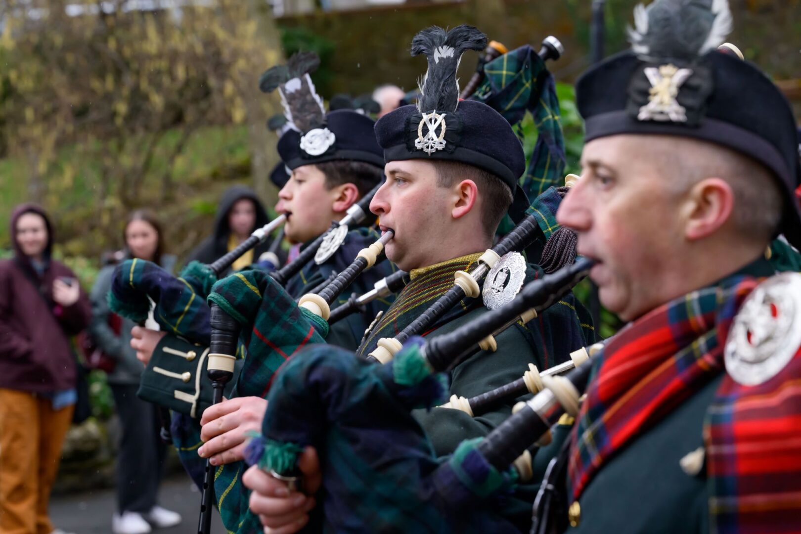 Row of people playing bagpipes and dressed in traditional Scottish dress.