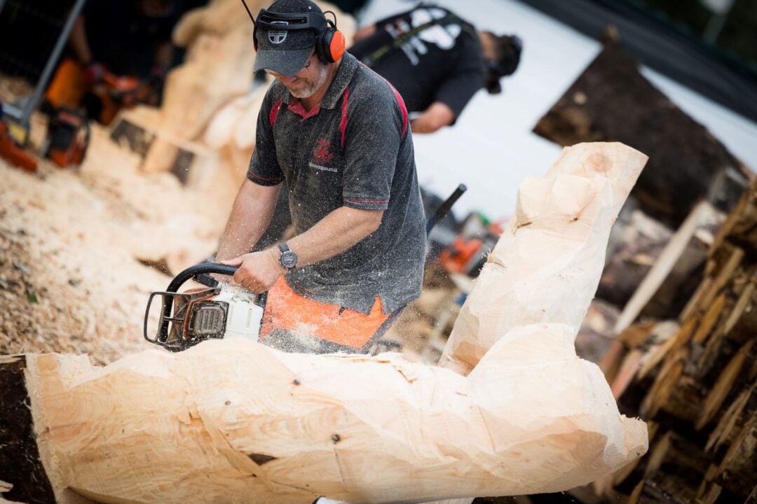 Man using a chainsaw to carve a large tree trunk.