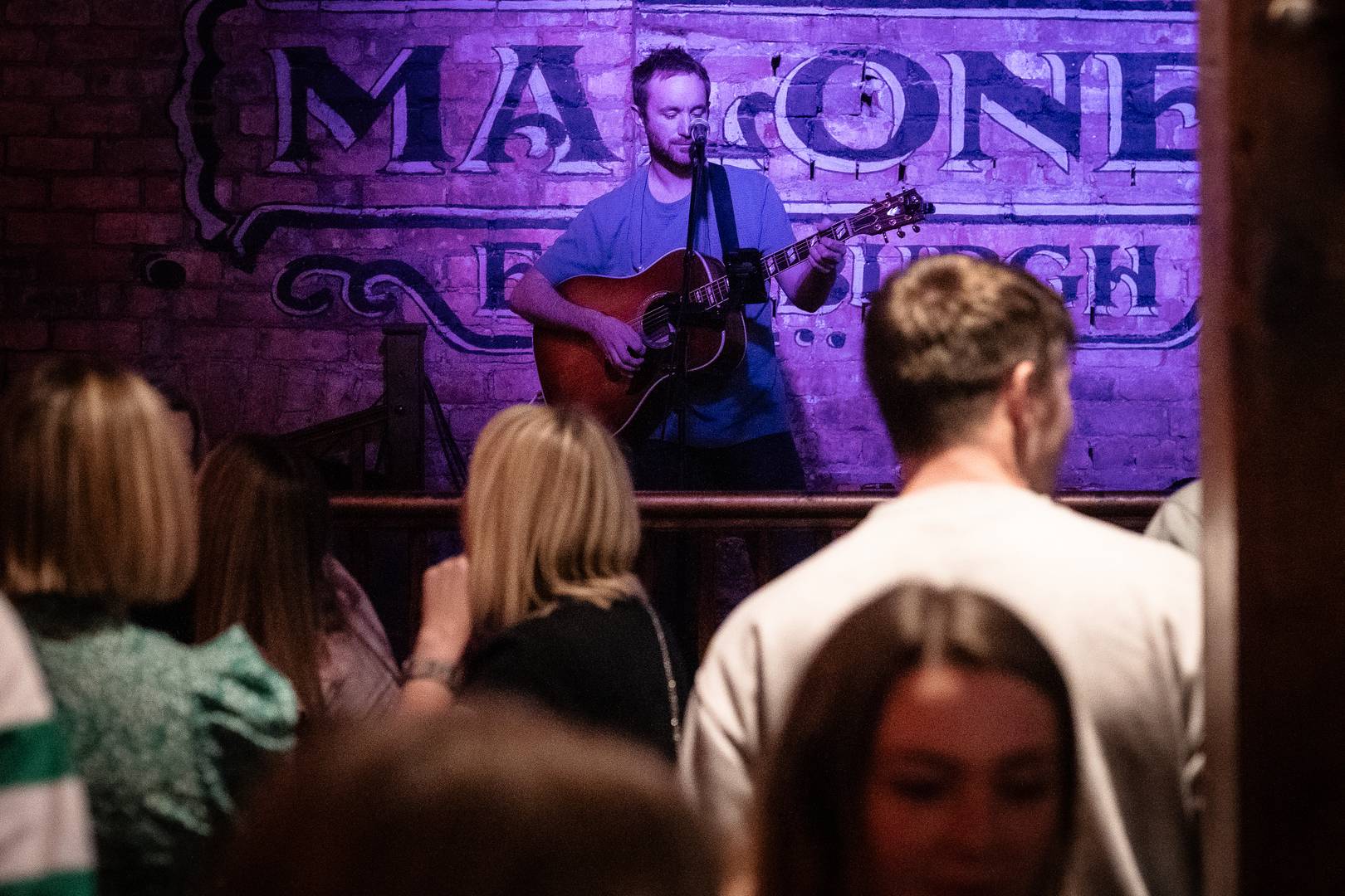 Singer and guitarist performs on pub stage in front of crowd,© Malones Edinburgh