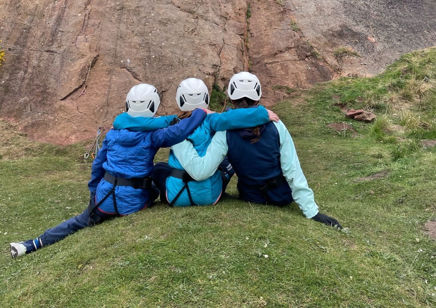 3 people sitting waiting for turn to climb rockface