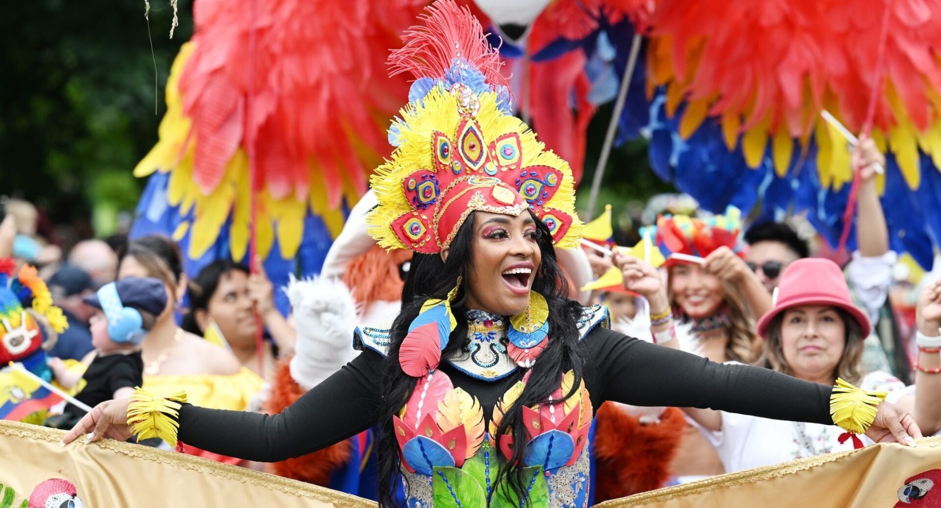 Women wearing a flamboyant costume and headdress standing in a crowd of people.